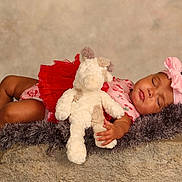 Saylor is registered to the contest to win money with this photo: baby, sleeping, toddler, stuffed_animal, pink_bow, red_skirt, furry_blanket, stone_surface, neutral_background, cute, child, resting, portrait, soft_texture, indoors, peaceful, infant, clothing, headband, hand