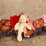 baby, sleeping, toddler, stuffed_animal, pink_bow, red_skirt, furry_blanket, stone_surface, neutral_background, cute, child, resting, portrait, soft_texture, indoors, peaceful, infant, clothing, headband, hand