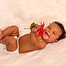 baby, infant, flower, smiling, happy, diaper, curly_hair, skin, cute, lying_down, white_background, soft_texture, child, holding, red_flower, portrait, one_person, indoors, playful, joyful
