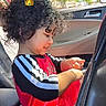 bracelet, car_interior, car_seat, casual, child, curly_hair, cute, daylight, digital_crown, happy, playing, red_clothing, seatbelt, side_profile, smiling, sunlight, trees, vehicle, window, young_child