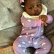 Jazmine joined the competition — help win amazing prizes! baby, infant, child, onesie, purple_clothing, hearts_pattern, pink_bow, hair_accessory, curly_hair, blanket, soft_texture, couch, indoor, portrait, cute, hands, face, expression, sitting, young