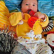 Rayyan joined the competition — help win amazing prizes! baby, child, toy, ladybug, rattle, yellow_sweater, patterned_pants, striped_blanket, stuffed_animal, tinsel, chewing, lying_down, colorful, playful, cute, infant, hand, face, smiling, indoors