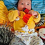 baby, child, toy, ladybug, rattle, yellow_sweater, patterned_pants, striped_blanket, stuffed_animal, tinsel, chewing, lying_down, colorful, playful, cute, infant, hand, face, smiling, indoors