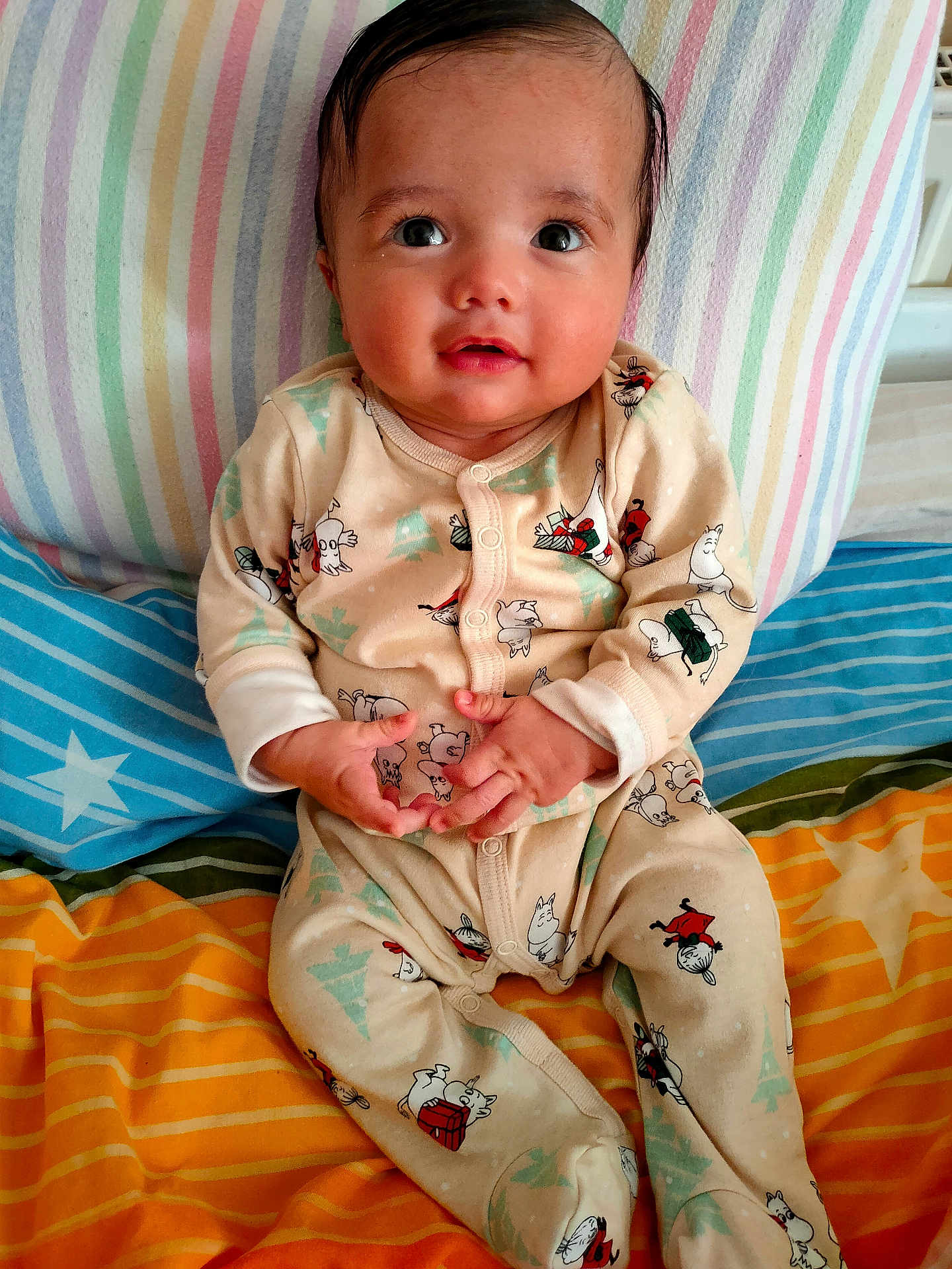 Rayyan is registered to the contest to win money with this photo: baby, infant, child, pajamas, striped_pillow, striped_blanket, bed, cute, indoors, portrait, smiling, hands, face, eyes, hair, sitting, clothing, cozy, resting, young_child