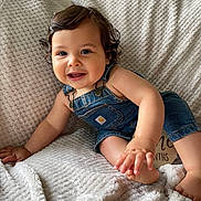 Crew is registered to the contest to win money with this photo: baby, child, denim_overalls, smiling, curly_hair, blanket, texture, indoors, cute, happy, person, infant, skin, hand, foot, portrait, sitting, cozy, comfortable, clothing