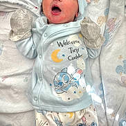 Hendrix joined the competition — help win amazing prizes! baby, newborn, yawning, blue_clothing, mittens, bunny_ears, sleepy, cute, infant, blanket, patterned_pajamas, lying_down, cozy, soft_lighting, indoors, child, adorable, cute_expression, small_hands, resting