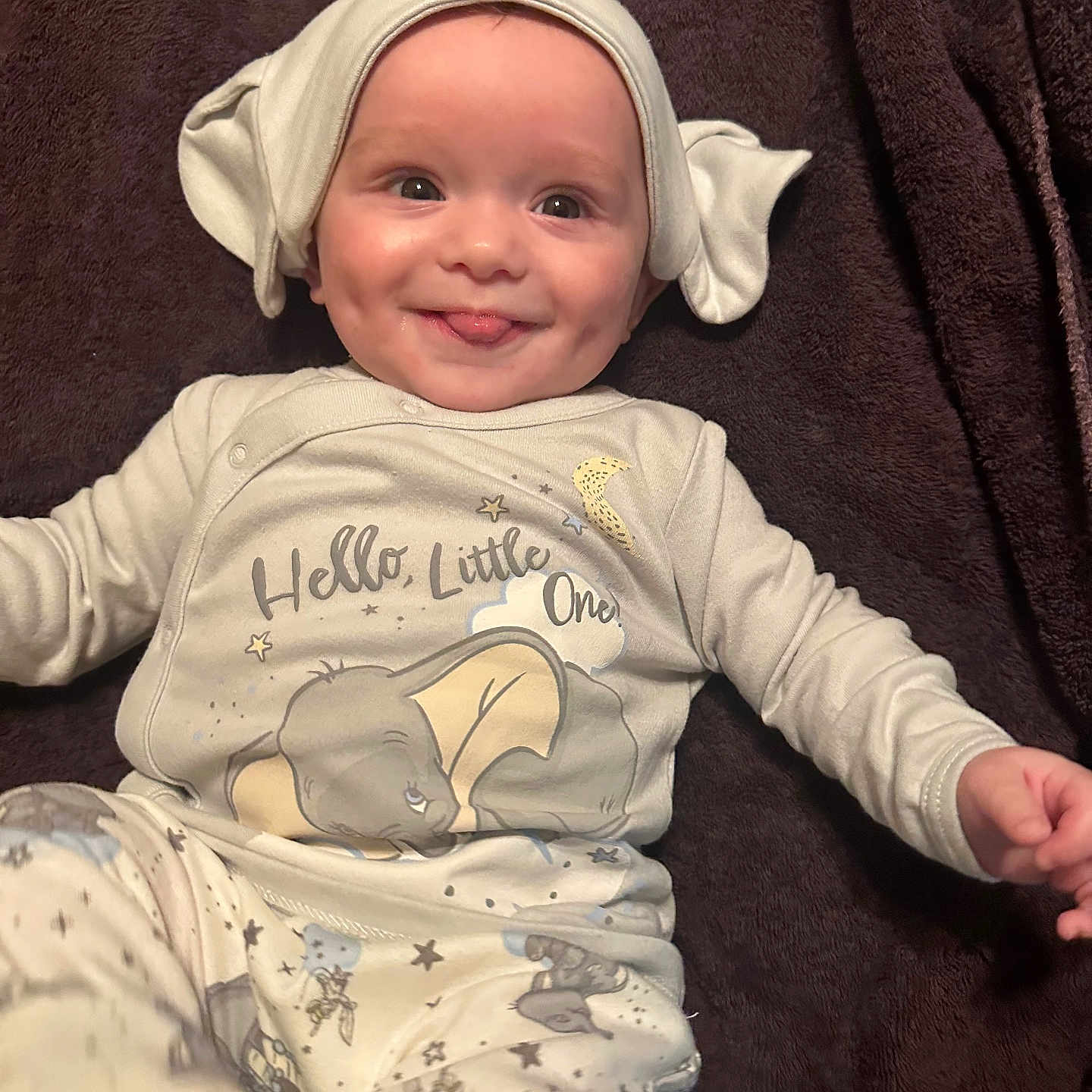 Hendrix is registered to the contest to win money with this photo: baby, infant, smile, tongue_out, elephant_hat, elephant_print, onesie, cute, soft_blanket, lying_down, happy, child, sleepwear, dimples, headwear, playful, indoors, portrait, young_child, person