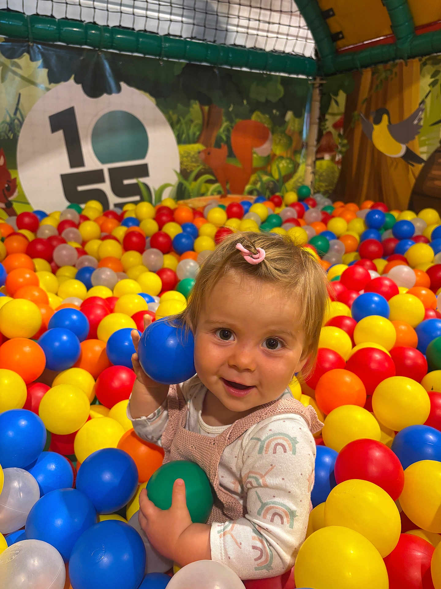 Anna a rejoint le concours — aidez-le/la à gagner de superbes lots ! child, toddler, ball_pit, colorful_balls, blue_ball, green_ball, pink_hair_clip, play_area, indoor, smiling, happy, cute, playful, forest_mural, squirrel, bird, long_sleeve_shirt, overalls, young_child, fun