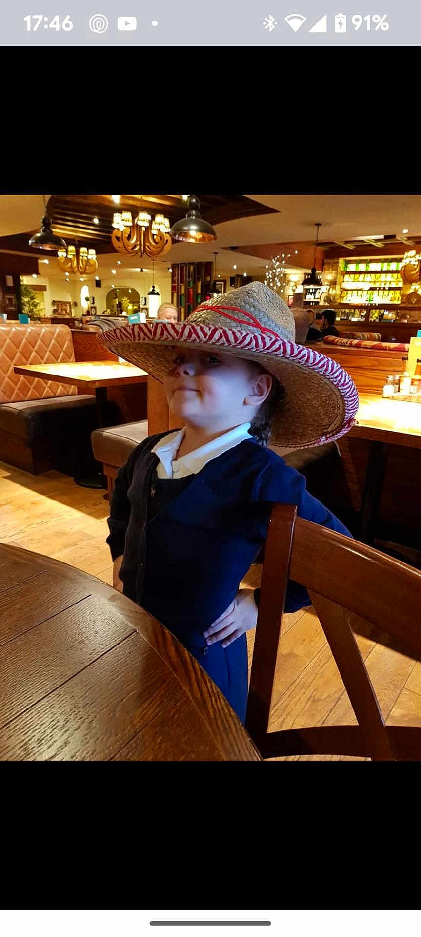 Jeru joined the competition — help win amazing prizes! child, sombrero, hat, restaurant, wooden_table, wooden_chair, lighting, indoor, pose, confident, furniture, person, casual_clothing, smile, decor, ceiling_lamp, table, flooring, background_people, cozy