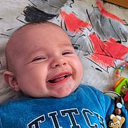 Ayden Weigel participe au concours pour gagner de l'argent avec cette photo : accessory, baby, beaded_toy, bedding, blue_shirt, closeup, crib, drooling, face, happy, indoors, infant, lying_down, mouth, pattern, rattle, smiling, stitch_character, teeth, toy