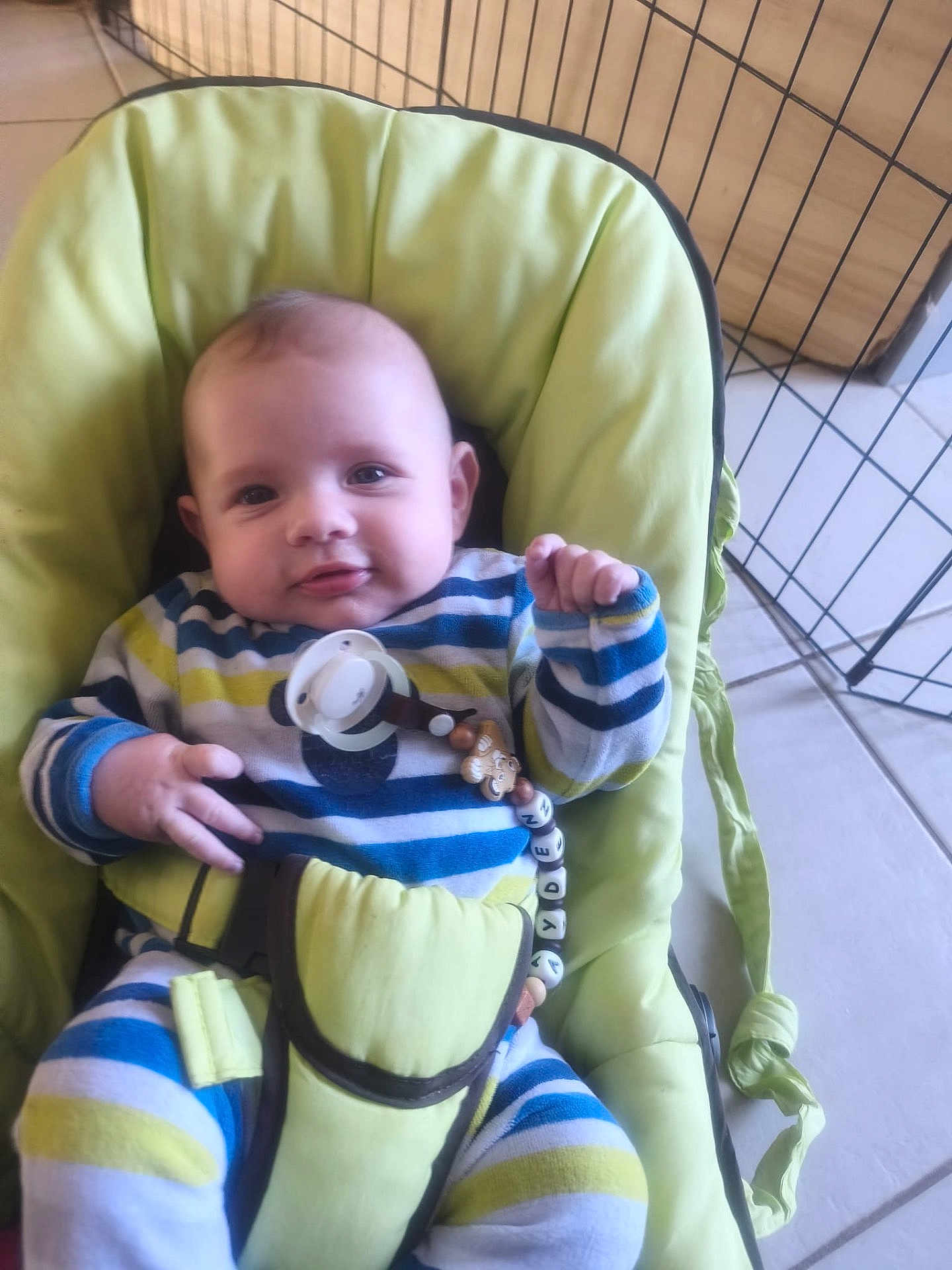 Ayden Weigel a rejoint le concours — aidez-le/la à gagner de superbes lots ! baby, bouncer, cushion, cute, eyes, face, floor_tiles, hand, head, indoor, infant, metal_grid, pacifier, pacifier_clip, playpen, seat_belt, smile, striped_clothes, striped_pajamas, toy_beads