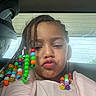 child, girl, braids, beads, colorful, selfie, car, car_seat, window, pouting, hair, portrait, clothing, pink_jacket, sunlight, happy, cute, casual, indoors, person