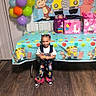toddler, birthday_party, curious_george, balloons, gift_bags, colorful, tablecloth, overalls, pink, white, beads, hair, floor, standing, indoor, child, smiling, celebration, party, decorations