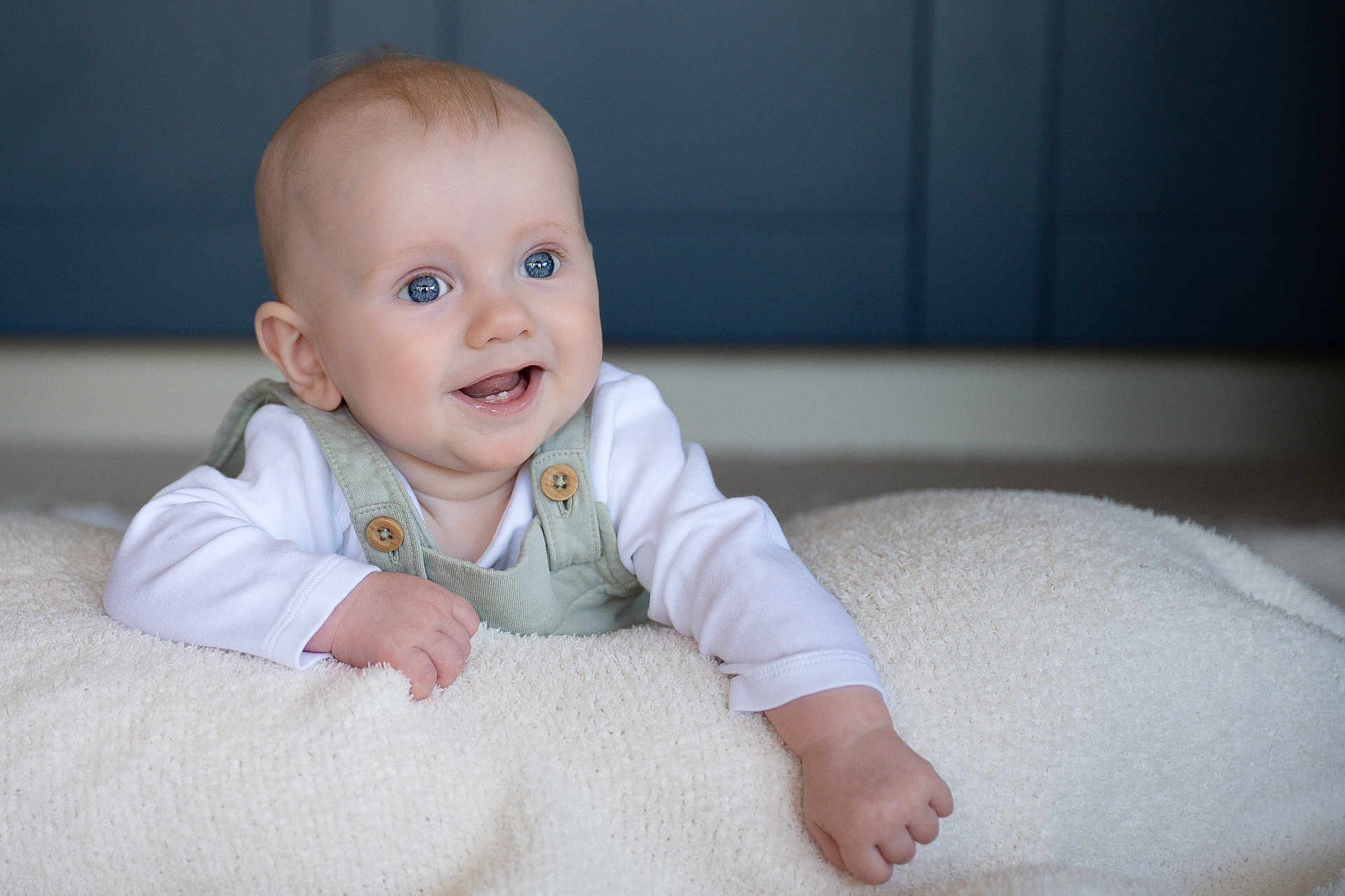 Theo joined the competition — help win amazing prizes! baby, child, smiling, blue_eyes, white_shirt, green_overalls, blanket, soft_texture, happy, cute, portrait, infant, indoor, cozy, young_child, face, hand, lying_down, expression, skin