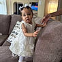 Meadow joined the competition — help win amazing prizes! toddler, child, white_dress, indoor, couch, sofa, hand, curious, standing, home, soft_lighting, blurred_background, person, footwear, baby_shoes, decor, living_room, cute, exploration, support