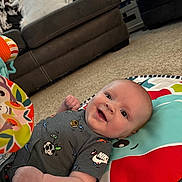 Myles joined the competition — help win amazing prizes! baby, infant, smile, play_mat, toy, onesie, carpet, couch, living_room, window_blinds, pillow, blanket, face, eyes, arm, hand, indoor, happy, cute, clothing