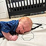 baby, baby_mat, blanket, blue_shirt, carpet, crib, crib_bars, door, door_knob, ear, hand, head, infant, mattress, nursery, playtime, portrait, shark_print, smiling, tummy_time