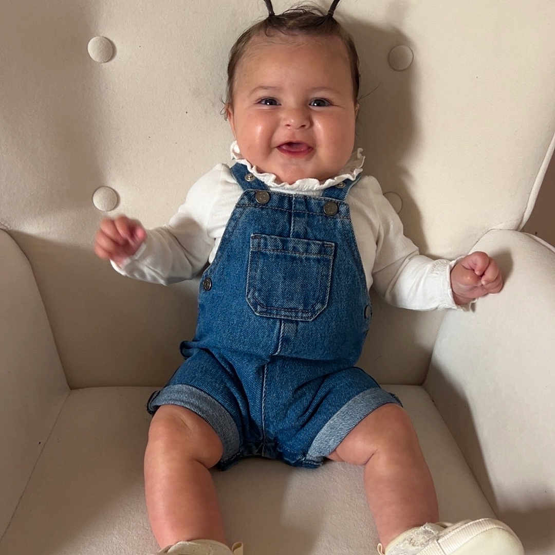 Alix a rejoint le concours — aidez-le/la à gagner de superbes lots ! armchair, baby, child, clothing, cozy, cute, denim_overalls, face, furniture, hair_tufts, happy, indoor, infant, legs, portrait, seated, skin, small_hands, smiling, white_shoes