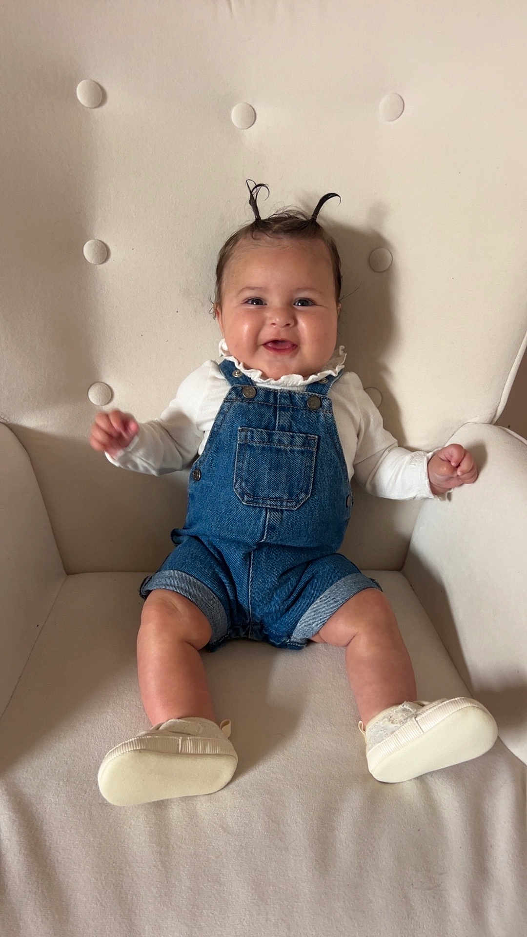 Alix a rejoint le concours — aidez-le/la à gagner de superbes lots ! baby, child, denim_overalls, white_shoes, armchair, smiling, happy, cute, indoor, seated, hair_tufts, clothing, infant, face, furniture, portrait, small_hands, legs, skin, cozy
