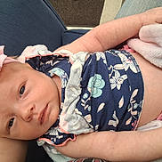 Taylin is registered to the contest to win money with this photo: baby, infant, child, face, eyes, smiling, portrait, floral_clothing, dress, headband, pink_flower, arms, adult, holding, blanket, cuddling, indoor, seated, closeup, family