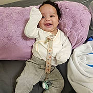 Yanasi is registered to the contest to win money with this photo: baby, infant, child, smiling, happy, portrait, sitting, lying_down, blanket, lavender, couch, clothing, onesie, pants, pacifier, toy, indoor, close_up, face, photography
