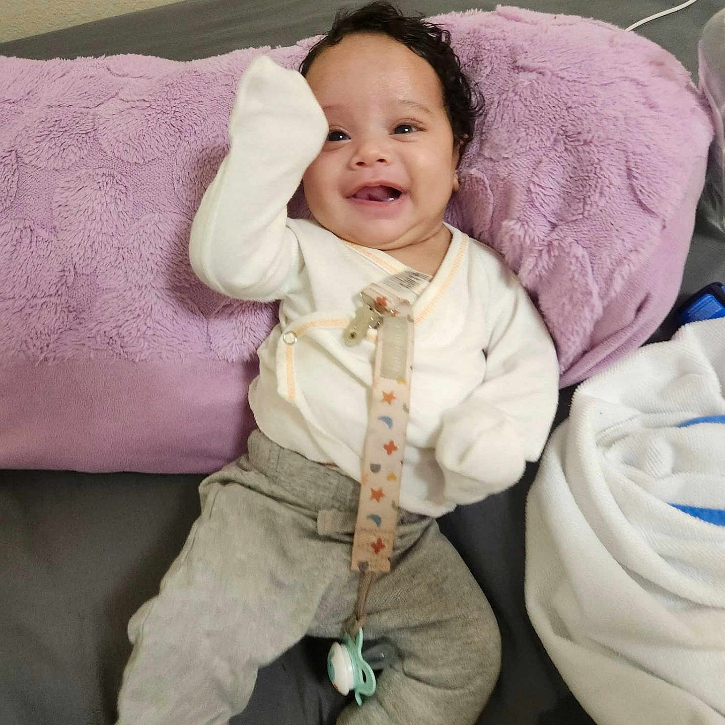 Yanasi is registered to the contest to win money with this photo: baby, infant, child, smiling, happy, portrait, sitting, lying_down, blanket, lavender, couch, clothing, onesie, pants, pacifier, toy, indoor, close_up, face, photography