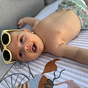 Jules participe au concours pour gagner de l'argent avec cette photo : arm, baby, blanket, child, clothing, cute, expression, face, happy, head, indoor, infant, lying_down, pattern, person, portrait, skin, smile, sunglasses, young