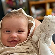 Jules participe au concours pour gagner de l'argent avec cette photo : baby, smiling, blanket, hood, stuffed_animal, toy, sheep, plush, face, infant, cute, child, portrait, cozy, happy, person, indoors, soft, closeup, warm