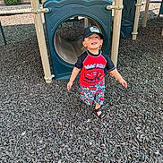 David is registered to the contest to win money with this photo: toddler, child, playground, slide, plastic, cap, sandals, smiling, outdoor, wood_chips, play_equipment, shorts, tshirt, person, daylight, fun, recreation, happy, young_child, casual_clothing