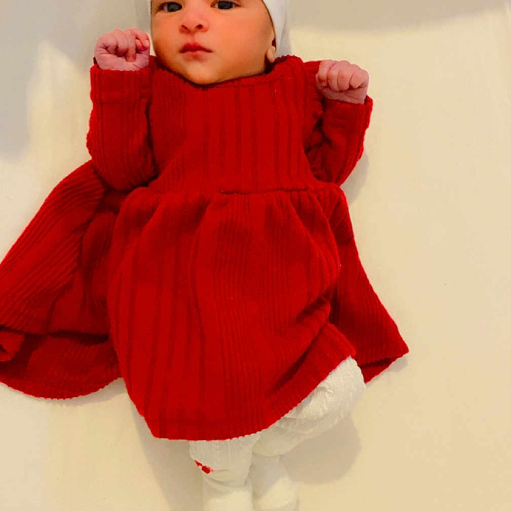 Dilnaaz is registered to the contest to win money with this photo: adorable, baby, baby_fashion, baby_hat, child, cute, indoor, infant, knitted_clothing, lying_down, newborn, peaceful, portrait, raised_fists, red_dress, small_hands, soft_surface, white_background, white_hat, white_socks