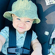 Logan is registered to the contest to win money with this photo: baby, child, bucket_hat, car_seat, blue_eyes, smiling, straps, clothing, cute, infant, face, hand, safety, seat_belt, expression, portrait, person, outdoor, happy, closeup