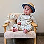 baby, child, hat, plush_toy, chair, furniture, indoor, cute, infant, portrait, expression, wooden_armrest, foot, floor_tile, wall, soft_texture, sitting, clothing, toy, curious
