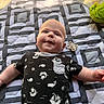 Orion is registered to the contest to win money with this photo: baby, infant, smile, onesie, patterned_clothing, quilt, blanket, indoor, child, cute, face, happy, lying_down, playtime, soft_toy, geometric_pattern, person, young_child, head, skin