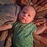 baby, infant, green_onesie, dinosaur_pattern, blanket, bedspread, lying_down, indoor, child, cute, face, head, arm, clothing, soft, portrait, curious, skin, person, baby_girl_or_boy