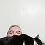 animal, black_and_white_cat, cable, casual, cat, close_up, comfort, companion, face, furry, hair, human, indoor, man, pet, portrait, relaxed, resting, sleeping_cat, white_wall