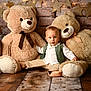 baby, teddy_bear, stuffed_animal, child, plush_toy, lantern, wooden_crate, brick_wall, star_decoration, flooring, vest, white_shirt, beige_pants, barefoot, indoor, portrait, smile, cute, cozy, warm_lighting