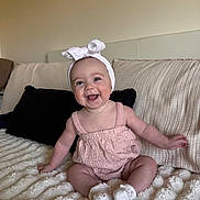 Lucy joined the competition — help win amazing prizes! baby, infant, child, smiling, headband, pink_outfit, sitting, blanket, couch, pillow, indoors, happy, cute, portrait, young_child, soft_texture, cozy, person, toddler, head