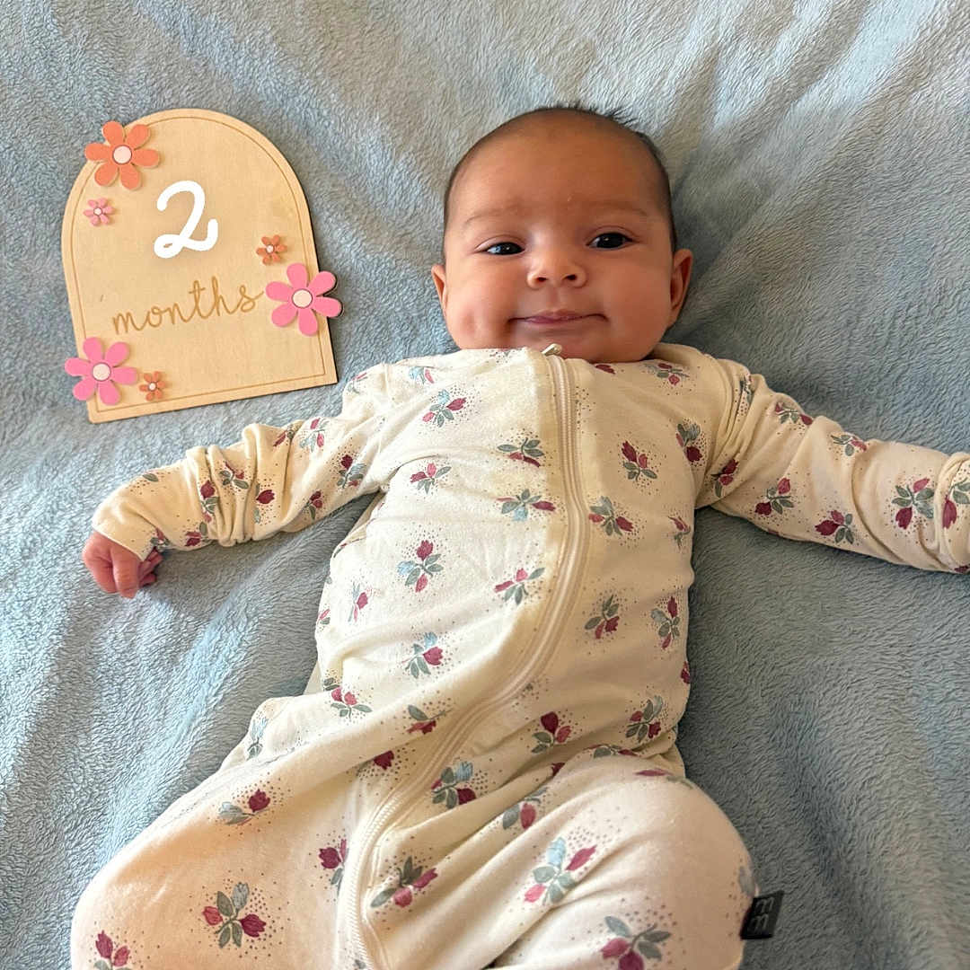 Alora joined the competition — help win amazing prizes! baby, infant, smiling, lying_down, blanket, onesie, floral_pattern, milestone, age_sign, cute, child, portrait, soft_texture, indoors, happy, peaceful, young_child, newborn, baby_clothes, decorative_sign