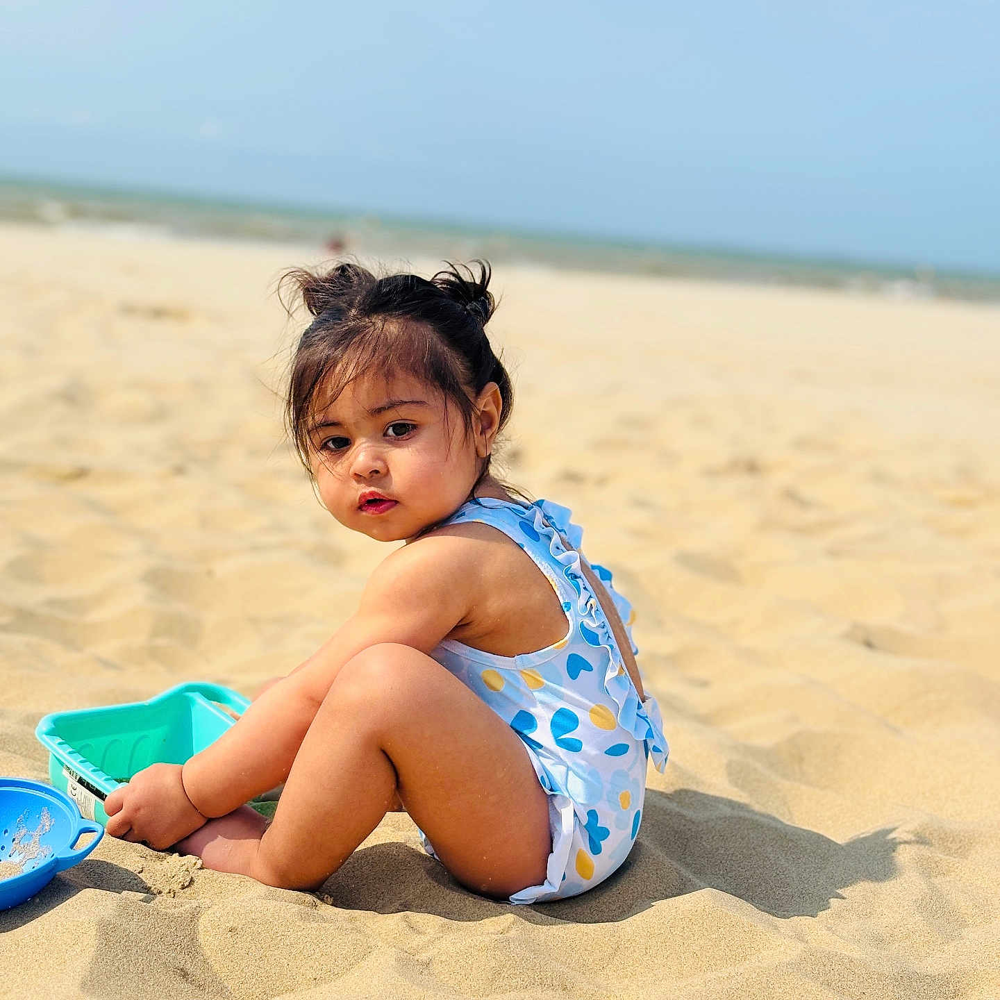 Haima participe au concours pour gagner de l'argent avec cette photo : beach, blue_sky, child, cute, hair_buns, nature, outdoor, playing, portrait, sand, sea, sitting, summer, sunlight, sunny, swimsuit, toddler, toys, vacation, water