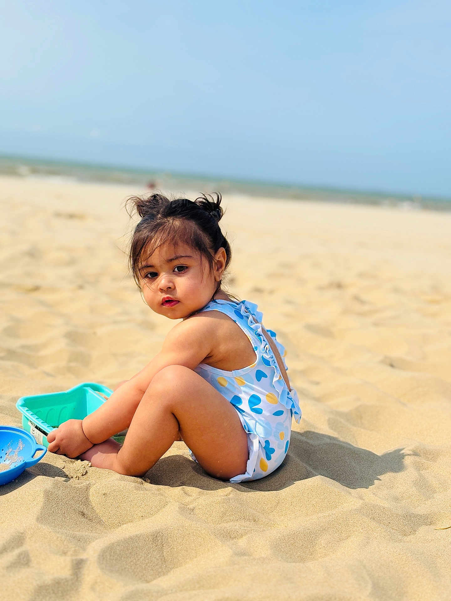 Haima participe au concours pour gagner de l'argent avec cette photo : toddler, child, beach, sand, sunny, playing, toys, swimsuit, hair_buns, outdoor, summer, cute, portrait, sitting, nature, water, sea, blue_sky, sunlight, vacation