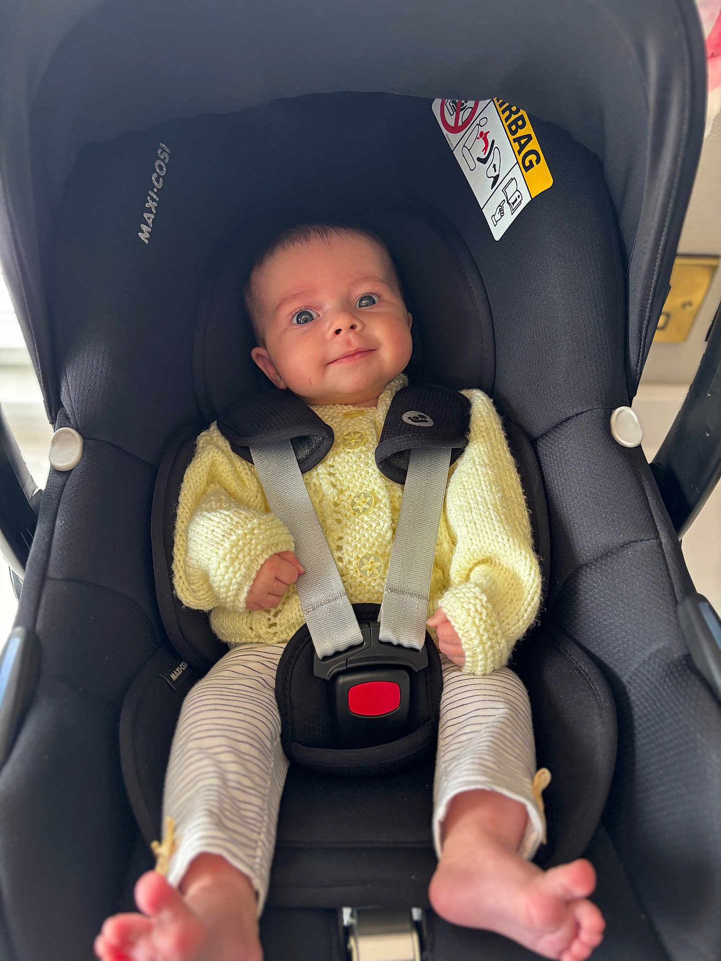 Isla is registered to the contest to win money with this photo: baby, car_seat, child, infant, smile, yellow_sweater, striped_pants, seatbelt, safety, indoors, cute, person, foot, head, face, knitted, clothing, straps, transport, happy
