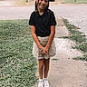 child, girl, smiling, outdoor, sidewalk, grass, black_polo_shirt, beige_skirt, white_sneakers, braided_hair, suburban, house, car, daylight, portrait, casual_clothing, standing, nature, happy, young