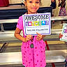 child, girl, award, certificate, pink_dress, heart_pattern, smiling, indoor, gymnasium, bench, celebration, achievement, medal, people, event, happy, school, standing, floor, long_hair
