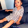 child, toddler, couch, remote_control, striped_clothing, indoor, furniture, person, relaxing, home, young_child, seated, living_room, casual, expressionless, short_sleeves, shorts, modern, comfort, technology