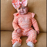 Ava is registered to the contest to win money with this photo: baby, child, bow, pink, outfit, couch, smile, sitting, cute, infant, clothing, white_socks, plaid, home, portrait, person, furniture, cozy, happy, young