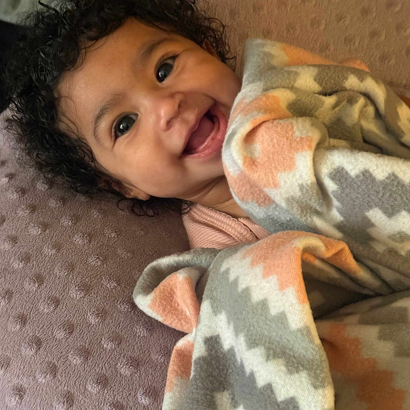 Nylah is registered to the contest to win money with this photo: baby, blanket, child, comfort, cozy, curly_hair, cute, expression, face, happy, indoors, infant, lying_down, patterned_blanket, person, smile, soft_texture, toddler, warm, wrapped