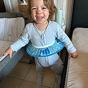 Enzo a rejoint le concours — aidez-le/la à gagner de superbes lots ! child, crib, curly_hair, face, floor_tile, furniture, hand_on_rail, happy, indoor, inflatable_ring, lamp, onesie, pajamas, playpen, portrait, smiling, standing, teeth, toddler, water_bottle