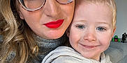 Charly a rejoint le concours — aidez-le/la à gagner de superbes lots ! woman, child, toddler, glasses, red_lipstick, smile, indoors, sweater, hoodie, family_photo, couch, toy, happy, portrait, closeup, person, face, hair, living_room, casual_clothing