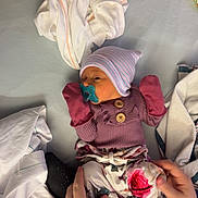 Oaklyn is registered to the contest to win money with this photo: baby, newborn, pacifier, mittens, striped_hat, floral_pants, hands, blanket, bed, clothing, soft_toys, infant, sleepy, resting, cute, comfort, warm, indoor, person, portrait