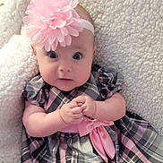 Freya is registered to the contest to win money with this photo: baby, child, infant, headband, flower, pink, dress, plaid, bow, hands, clasped, wide_eyes, blanket, soft, cute, portrait, indoors, person, young, cozy